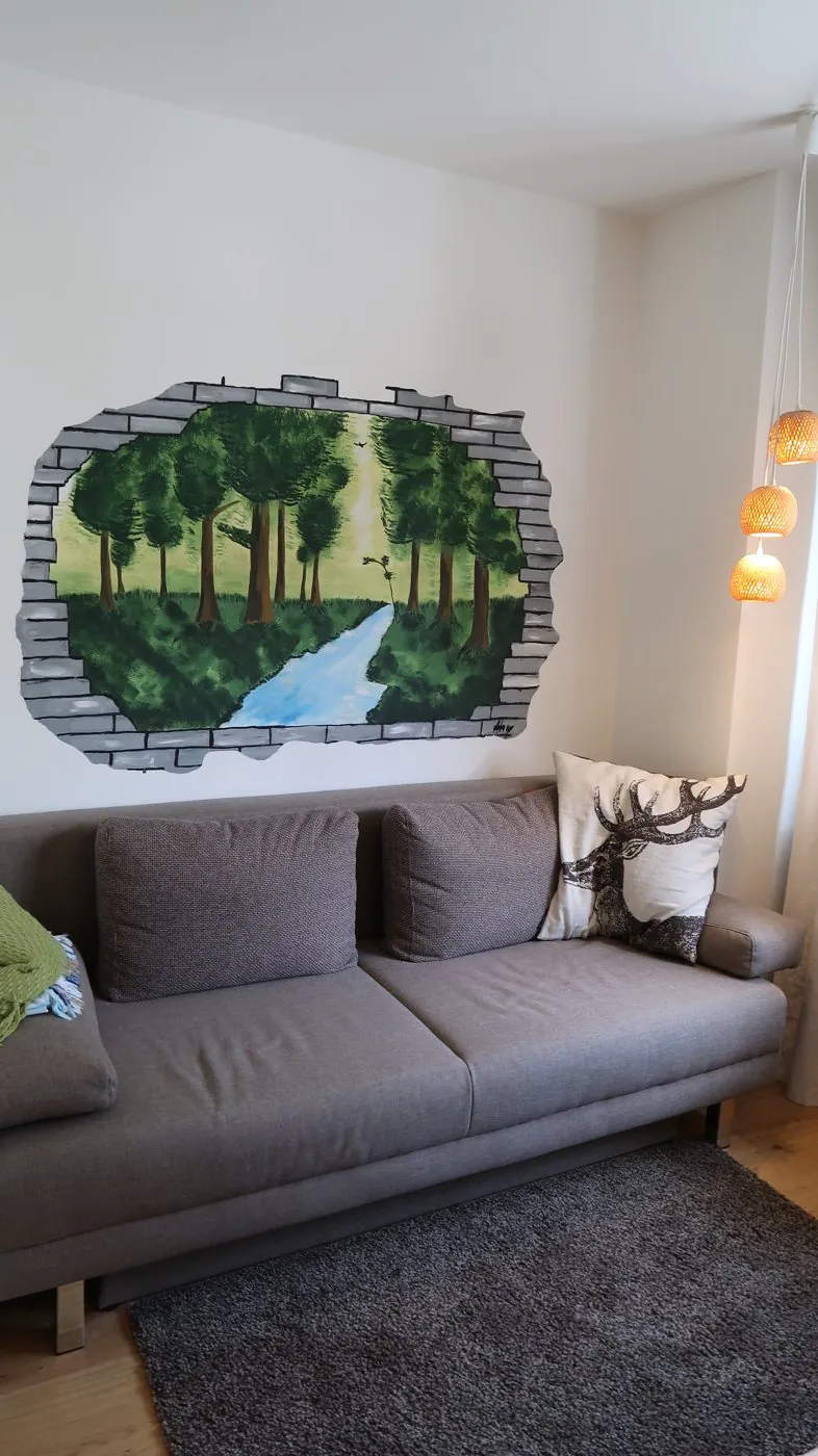 Wandbild im Praxisraum: ein Durchbruch in der Mauer mit Blick auf Wald und Bach